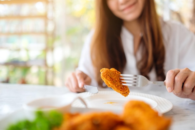 Nahaufnahmebild einer schönen asiatischen frau, die gebratenes hähnchen mit der gabel im restaurant isst