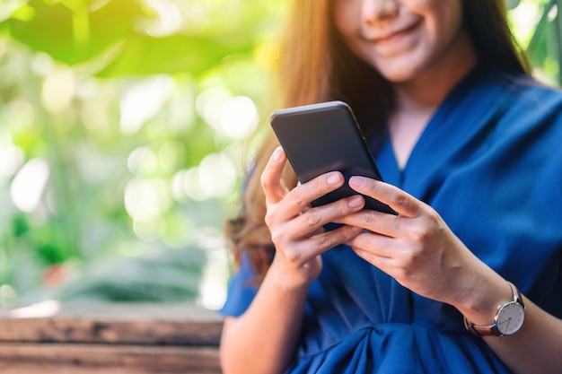 Nahaufnahmebild einer schönen asiatischen frau, die handy im garten hält, benutzt und betrachtet