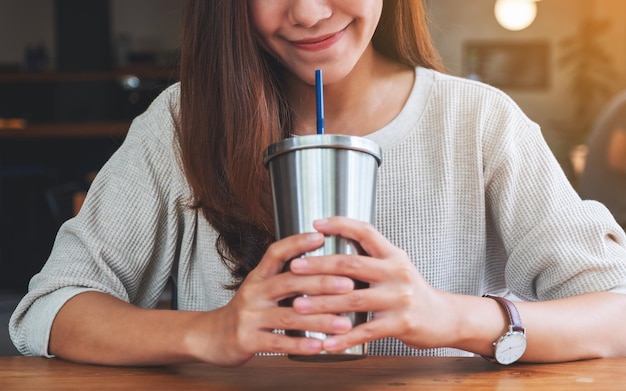 Nahaufnahmebild einer schönen asiatischen Frau, die Kaffee in der Edelstahlschale trinkt