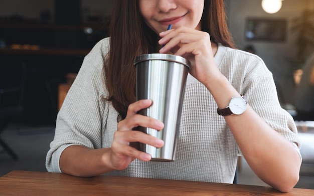 Nahaufnahmebild einer schönen asiatischen Frau, die Kaffee in der Edelstahlschale trinkt