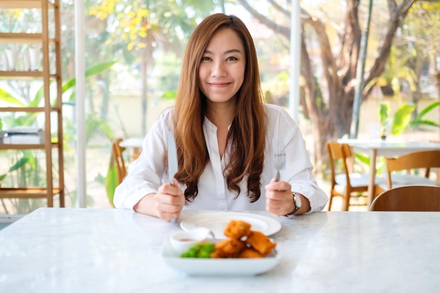 Nahaufnahmebild einer schönen asiatischen frau, die messer und gabel benutzt, um gebratenes hähnchen im restaurant zu essen?