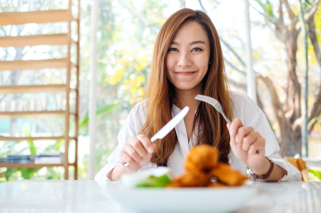 Nahaufnahmebild einer schönen asiatischen frau, die messer und gabel benutzt, um gebratenes hähnchen im restaurant zu essen?