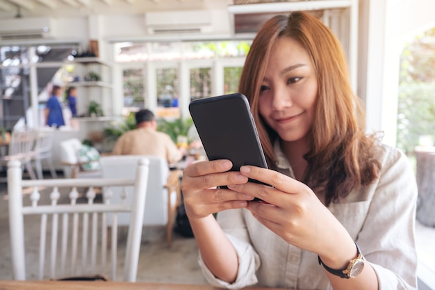 Nahaufnahmebild einer schönen Frau, die das Smartphone im Café hält, benutzt und betrachtet