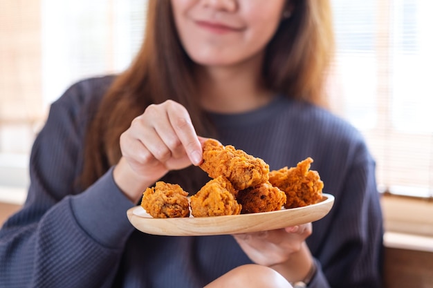 Nahaufnahmebild einer schönen jungen asiatischen Frau, die zu Hause gebratenes Huhn in der Küche hält und isst