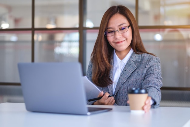 Nahaufnahmebild einer schönen jungen asiatischen Geschäftsfrau, die Kaffee trinkt und Laptop-Computer beim Arbeiten im Büro verwendet