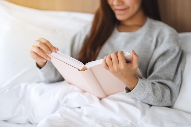 Nahaufnahmebild einer schönen jungen Frau, die Buch in einem weißen gemütlichen Bett zu Hause liest