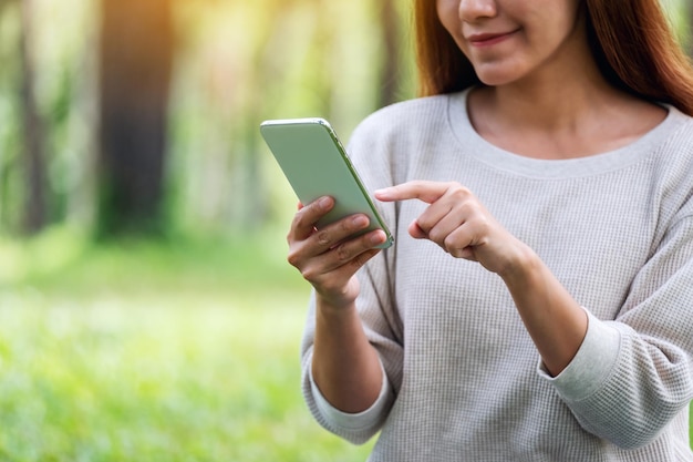 Nahaufnahmebild einer schönen jungen Frau, die Handy im Park hält und benutzt