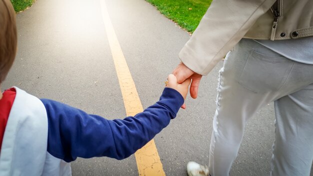 Nahaufnahmebild eines kleinen 3 Jahre alten Kleinkindjungen, der seine Mutter mit der Hand hält und im Park auf der Straße geht