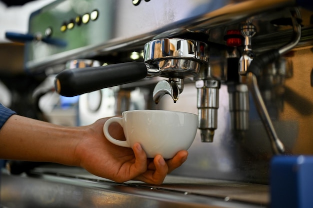 Nahaufnahmebild eines professionellen männlichen Baristas, der eine Tasse Cappuccino mit einer Espressomaschine zubereitet