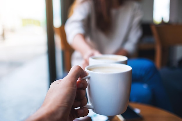 Nahaufnahmebild von Mann und Frau, die im Café mit weißen Kaffeetassen klirren