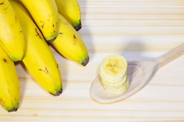 Nahaufnahmebündel Bananen auf Holztisch nahe bei Löffel mit geschnittener Frucht