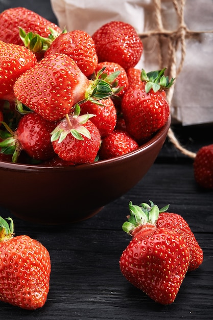 Nahaufnahmeerdbeeren in einer Tonplatte, dunkler Hintergrund, Lieferung, Bio-Produkte, Layout für eine gesunde Ernährung und Bio-Restaurant-Kochwerbung.