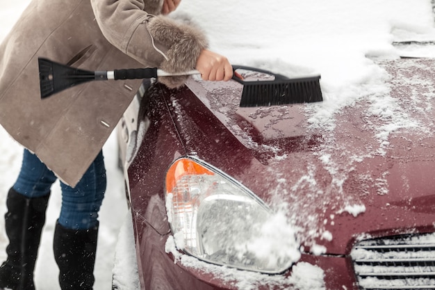 Nahaufnahmefoto der Frau, die Bürste hält und Schnee vom Auto säubert