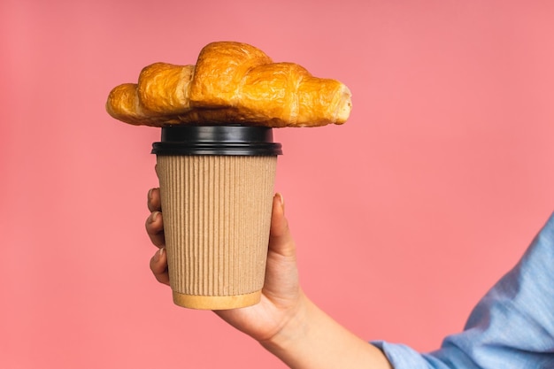 Nahaufnahmefoto der Hand der Frau, die Croissant hält Isoliertes Porträt der Frau mit Fast Food und einer Tasse Kaffee auf rosa Hintergrund Diät-Frühstückskonzept