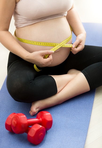 Nahaufnahmefoto der schwangeren Frau, die den Bauch mit Klebeband misst