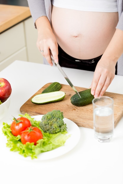 Nahaufnahmefoto der schwangeren Frau, die Gemüsesalat in der Küche macht