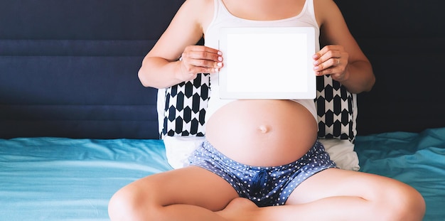 Nahaufnahmefoto der schwangeren Frau, die zu Hause einen leeren Tablet-Bildschirm hält und zeigt Mutter bei der Erwartung des Babys mit digitalem Tablet Schwangerschafts- und Technologiekonzept