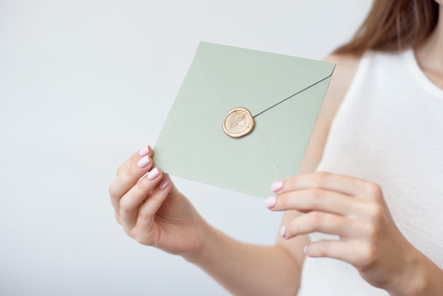 Nahaufnahmefoto der weiblichen Hände, die Einladungsumschlag mit einem Goldwachssiegel, Geschenkgutschein, Postkarte, Hochzeitseinladungskarte halten