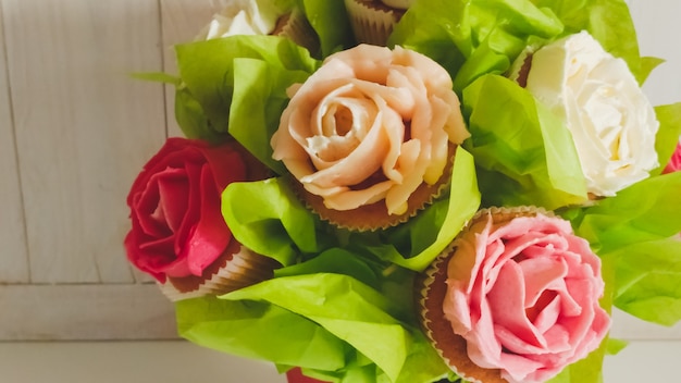 Nahaufnahmefoto des Blumenstraußes aus Kuchen und Cupcakes auf weißem Schreibtisch aus Holz. Schöne Aufnahme von Süßigkeiten und Gebäck auf weißem Hintergrund