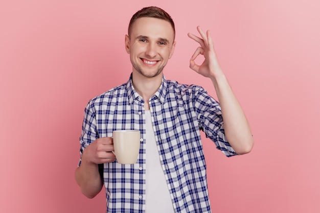 Nahaufnahmefoto des gutaussehenden jungen Mannes glückliches positives Lächeln halten Becherkaffee zeigen okayzeichengetränk lokalisierten Pastellhintergrund