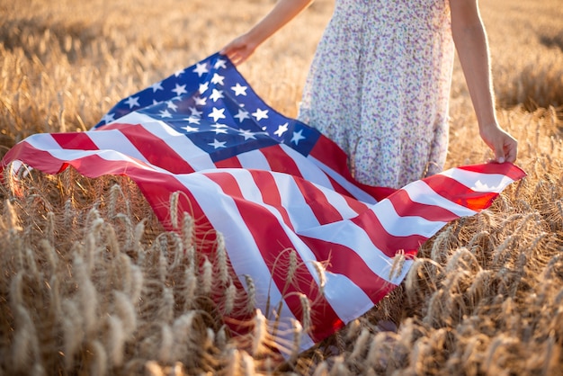 Nahaufnahmefoto des Mädchens, das Flagge der USA auf reifem Roggen oder Weizen hält. Unabhängigkeitstag der USA