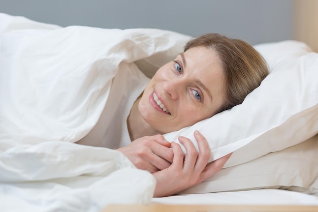 Nahaufnahmefoto des Porträts einer Frau, die im Bett schläft, lächelt und morgens in die Kamera schaut