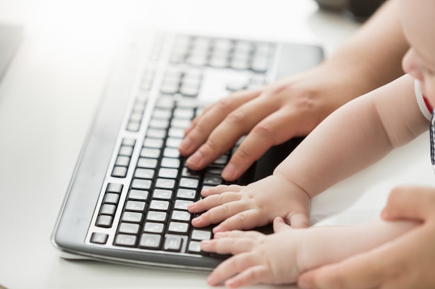 Nahaufnahmefoto des Vaters, der seinem Baby beibringt, wie man die Computertastatur benutzt