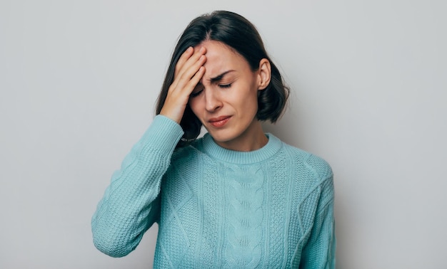 Nahaufnahmefoto einer jungen Frau, die ihren Kopf berührt, während sie an Migräne und Kopfschmerzen leidet Traurige und müde junge Frau, die die Stirn berührt, während sie Depressionen überarbeitet hat