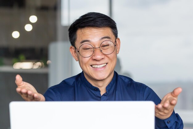 Nahaufnahmefoto eines erfolgreichen asiatischen Geschäftsmannes, der aus der Ferne bei einem Videoanruf spricht, männlicher Chef mit Brille