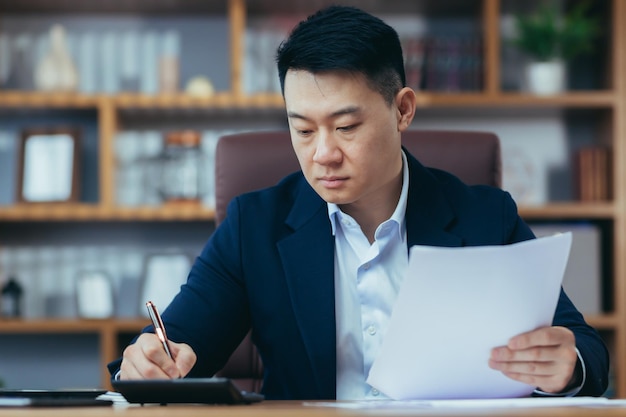 Nahaufnahmefoto eines Geschäftsmannes im Büro, der an Papier arbeitet, ernsthafter und konzentrierter asiatischer Chef, der Dokumente unterzeichnet