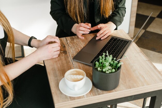 Nahaufnahmefoto eines Schreibtisches in einem Café mit einem Laptop, einer Tasse Kaffee und einem Blumentopf