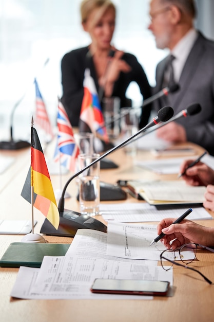 Nahaufnahmefoto, Fokus auf Mikrofone, Geschäftsleute, die vor Mikrofonen sitzen, während sie an der Pressekonferenz teilnehmen