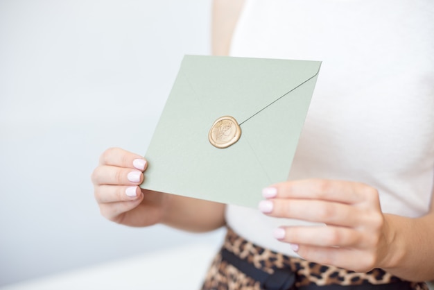 Nahaufnahmefoto von den weiblichen Händen, die Einladungsumschlag mit einem Wachssiegel, einem Geschenkgutschein, einer Postkarte, einer Hochzeitseinladungskarte halten.