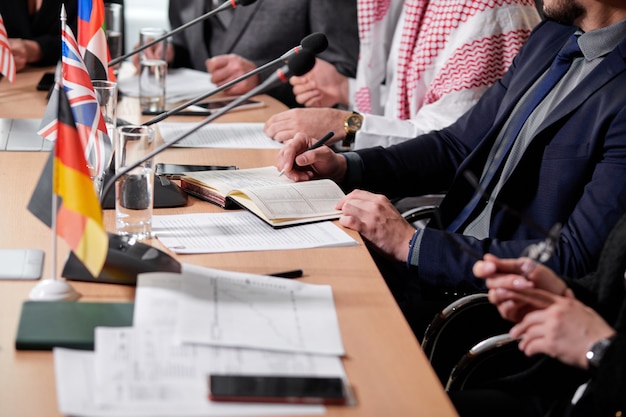 Nahaufnahmefoto von Führungskräften, die am Schreibtisch sitzen und Notizen machen, mit Dokumenten, Pressekonferenz. geschäftliches oder politisches Treffen im Sitzungssaal