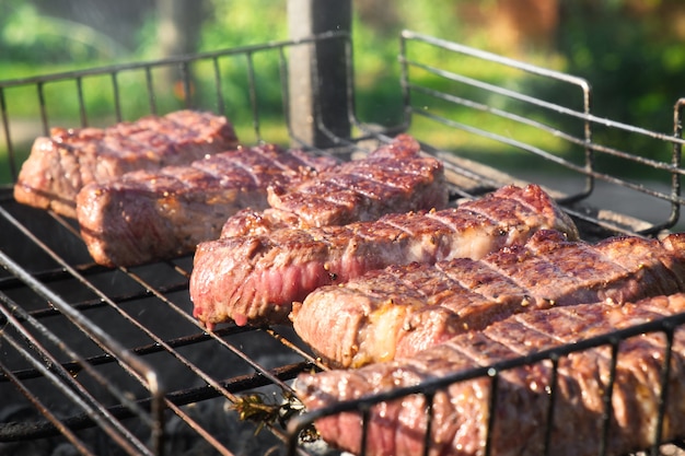 Nahaufnahmefoto von gegrilltem Fleisch auf einem Drahtgestell. Steaks grillen auf einem Kohlenbecken mit natürlichem Rauch. Kochen im Freien.