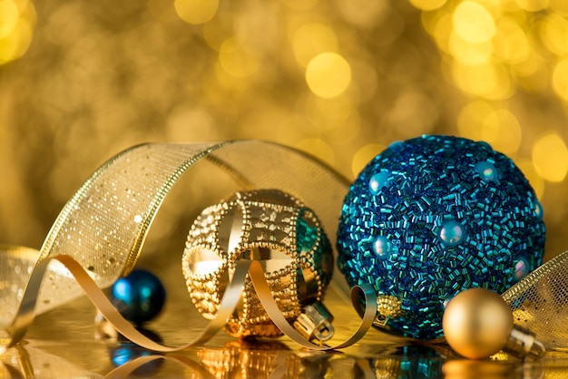 Nahaufnahmefoto von goldenen und blauen Christbaumschmuck-Ornamentenbällen Serpentin und Band auf glänzendem goldenem Bokeh-Hintergrund