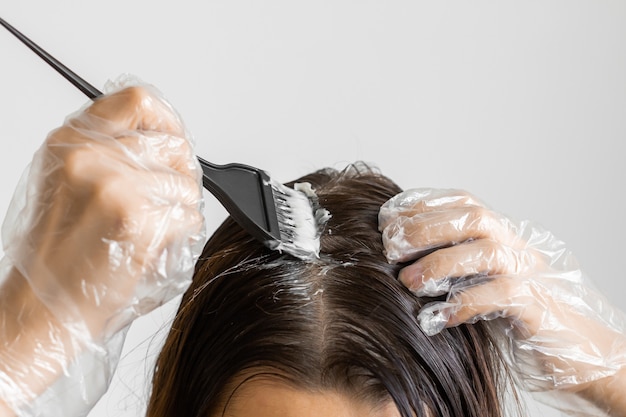 Nahaufnahmefrau Hände färbt Haare mit einem schwarzen Pinsel. Färbung von weißen Haaren zu Hause.