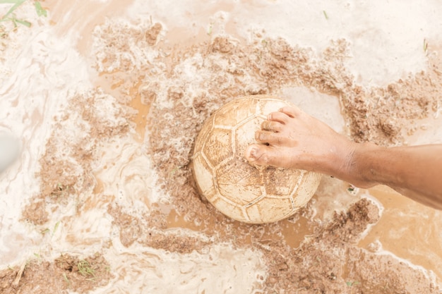 Nahaufnahmefußkind und -ball, die auf Schlamm spielen