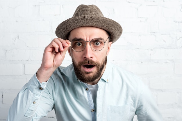 Foto nahaufnahmegesichtsporträt des bärtigen mannes im hut und in der brille suchen. emotionsüberraschung, empörung