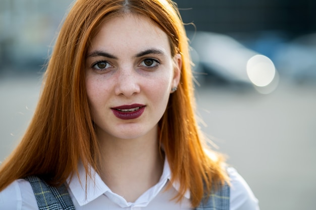 Nahaufnahmegesichtsporträt eines lächelnden Teenager-Mädchens mit roten Haaren und klaren Augen.
