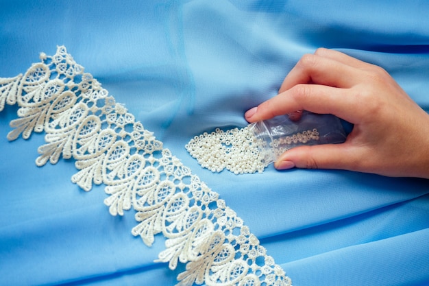 Foto nahaufnahmehände der schneiderin (schneiderin) designerin blaues chiffonkleid näht perlen zum spitzen auf blauem hintergrund im studio