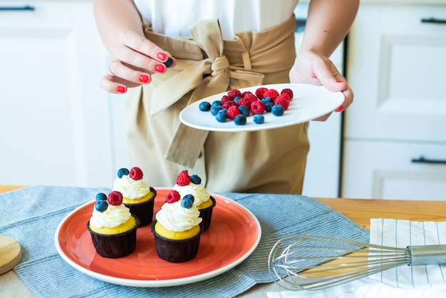 Nahaufnahmehände, die Cupcakes mit farbigen Beeren, Himbeeren und Blaubeeren verzieren. Lebensstil, zu Hause kochen