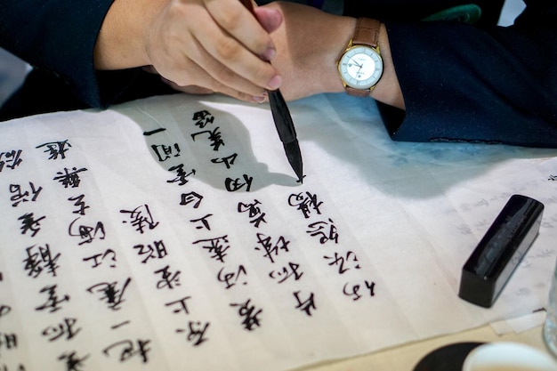 Nahaufnahmehände, die einen chinesischen Pinsel halten und chinesische Texte mit schwarzer Tinte auf ein Papier schreiben