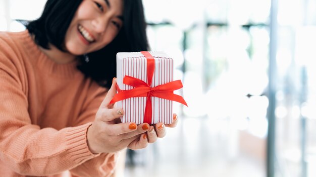 Nahaufnahmehände, die Geschenkbox der glücklichen lächelnden jungen Frau halten