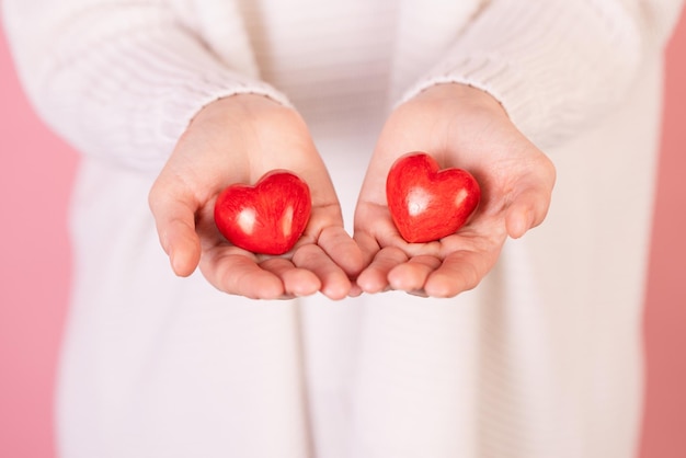 Nahaufnahmehände, die Herz auf rosafarbenem Hintergrund Valentinstagkonzept halten