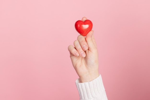 Nahaufnahmehände, die Herz auf rosafarbenem Hintergrund Valentinstagkonzept halten