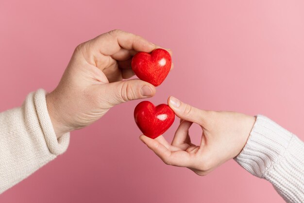 Nahaufnahmehände, die Herz auf rosafarbenem Hintergrund Valentinstagkonzept halten