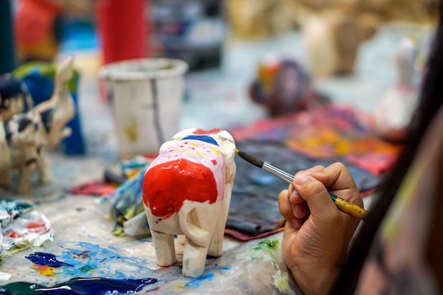 Nahaufnahmehände von den Kunststudenten, die Pinselstudie halten und Farbe auf hölzerner Tierpuppe im Kunstklassenzimmer lernen.