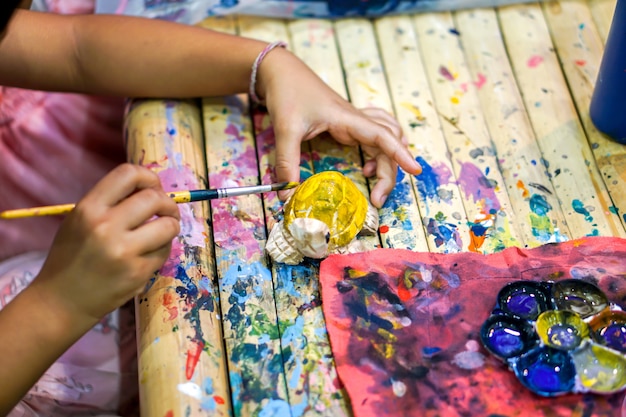 Nahaufnahmehände von den Kunststudenten, die Pinselstudie halten und Farbe auf hölzerner Tierpuppe im Kunstklassenzimmer lernen.