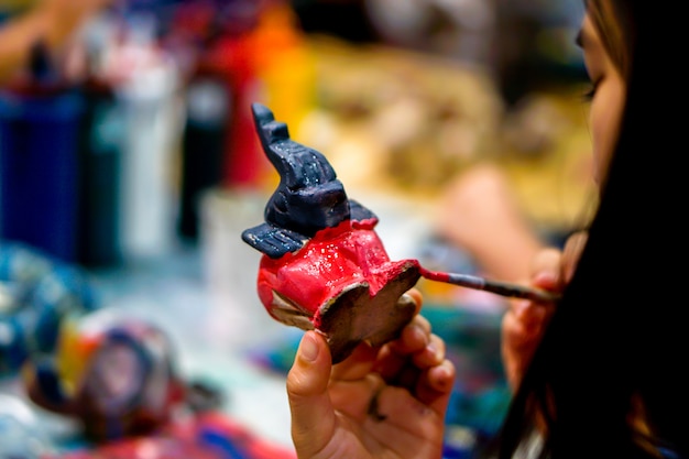 Nahaufnahmehände von den Kunststudenten, die Pinselstudie halten und Farbe auf hölzerner Tierpuppe im Kunstklassenzimmer lernen.